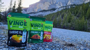 Vince food packages on a rocky surface with a mountainous background. Camping and tramping instant meals